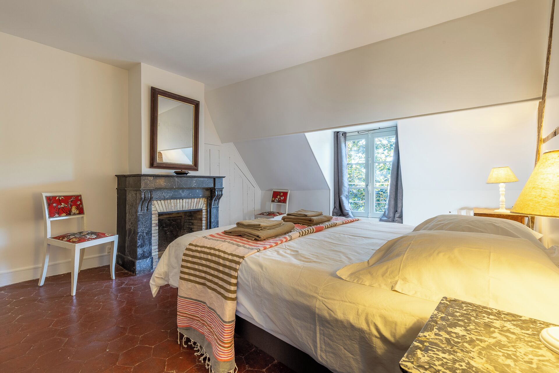 A bedroom with a bed, a fireplace, a chair, and a window.