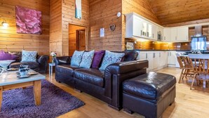 Interior acogedor de una cabaña con techo de madera, sofá de cuero, mesa de comedor y zona de cocina.