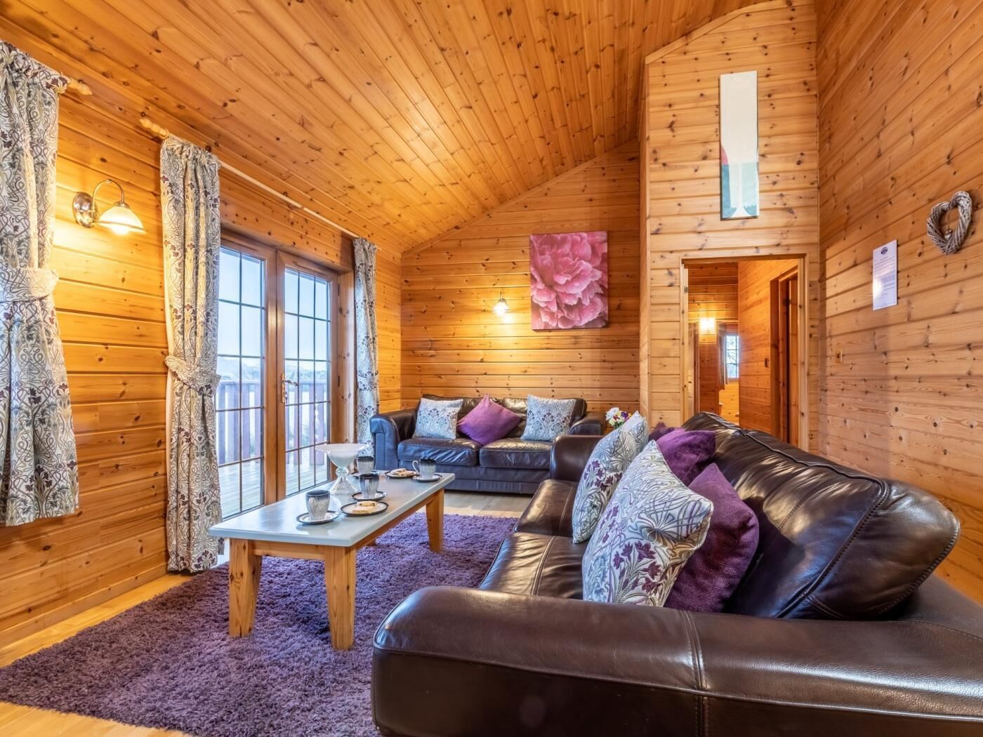 Interior acolhedor de uma cabana com teto de madeira, um sofá, uma mesa e uma janela grande.