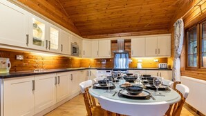 Una cocina con paneles de madera, armarios blancos, una estufa central y una mesa de comedor para seis personas con sillas.