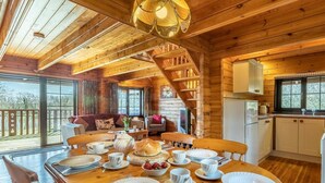A wooden cabin interior with a dining table set for four, a kitchen area, and a staircase leading to an upper level. - 3 Bed in Bideford (oc-00369) (Higher Clovelly)