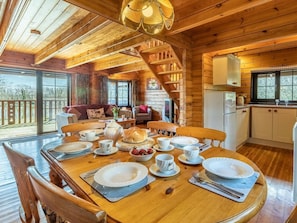 L’intérieur d’un chalet en bois comprend une salle à manger avec une table dressée pour quatre personnes, un coin cuisine et un escalier menant à l’étage supérieur.