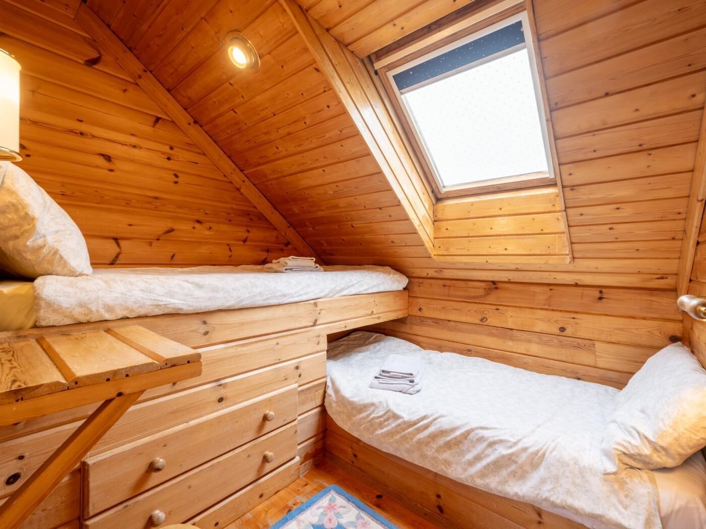 A small, wooden cabin room with two bunk beds, a window, and a wooden dresser.