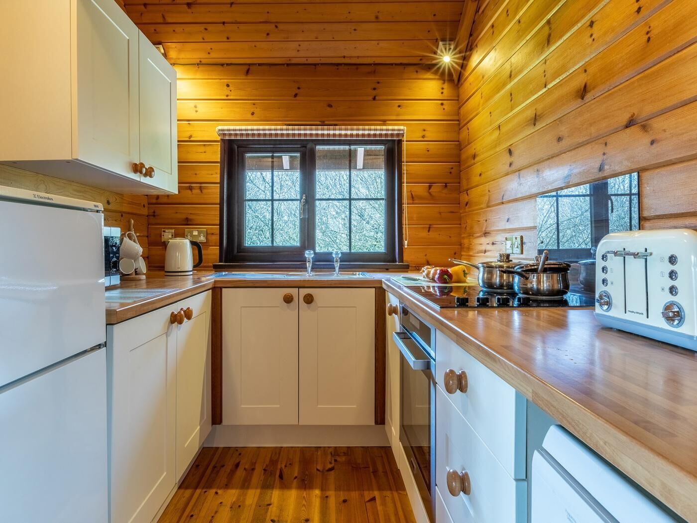 A compact kitchen with wooden walls, a window, a sink, and a stove.