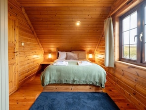 Une chambre à coucher dans une cabane en bois, avec un lit, deux lampes de chevet, une fenêtre et un tapis bleu.