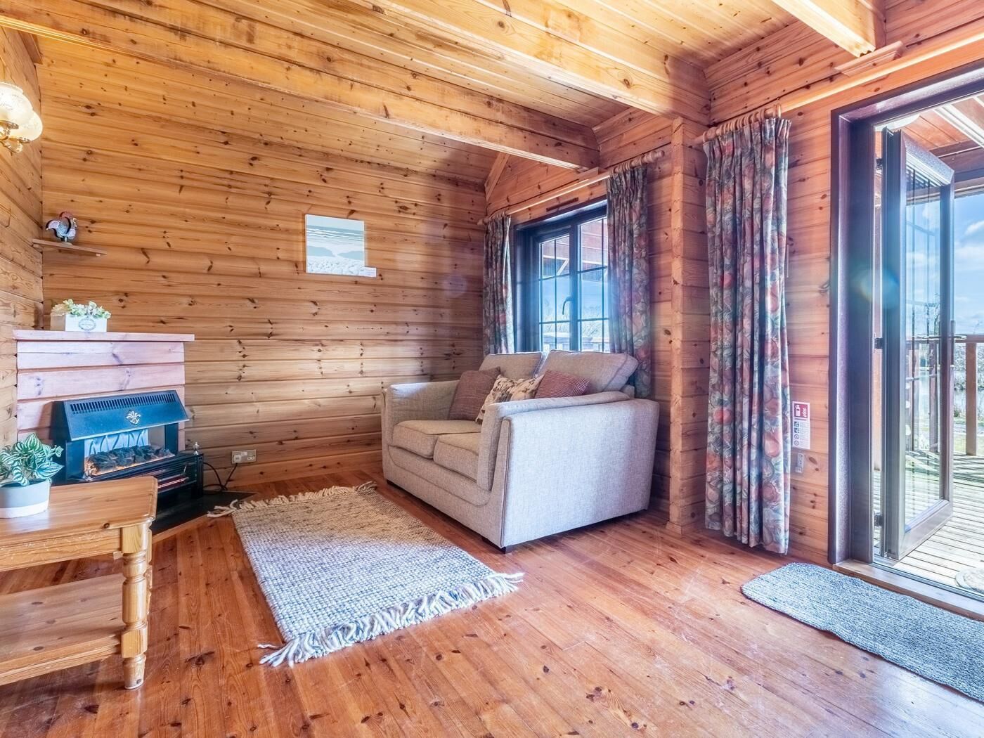 Interior acogedor de una cabaña con sofá, chimenea y un amplio ventanal.