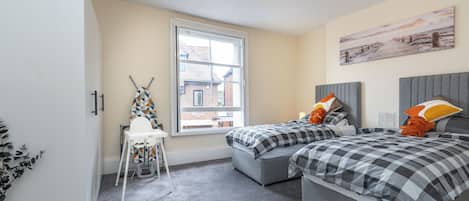 A bedroom with two beds, a window, a radiator, and a view of the outside.