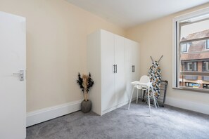 A room with a white wardrobe, a potted plant, a white chair, and a window with a view of buildings.