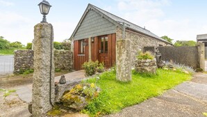 A stone house with a red door, a stone lamp post, and a garden with flowers and plants. - 2 Bed in Launceston (oc-congs) (Congdon's Shop)