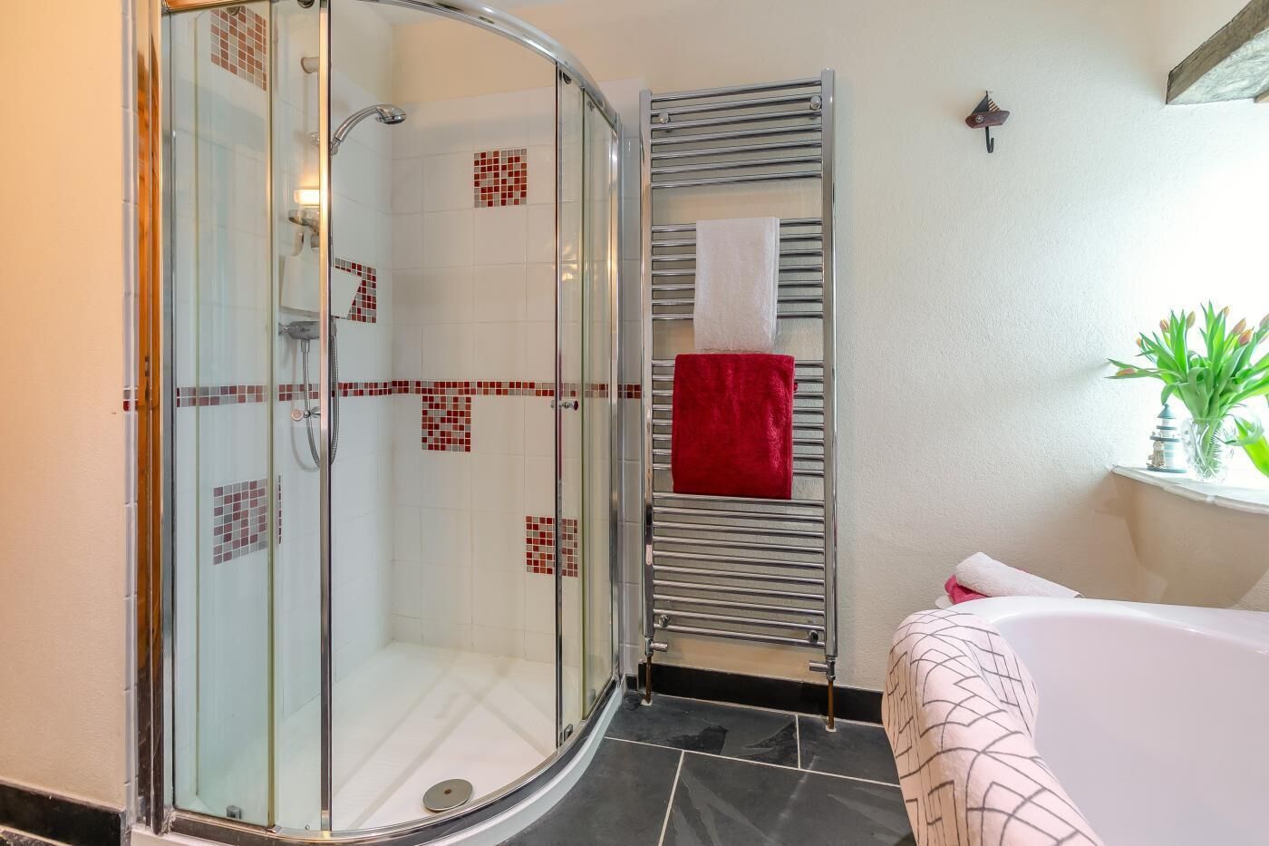 A bathroom with a glass-enclosed shower, a towel rack with a red towel, and a white bathtub.