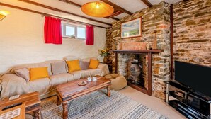 A cozy living room with a stone wall, a wooden sofa with cushions, a wooden coffee table, a fireplace, and a television. - 5 Bed in Bideford (oc-codar) (Westward Ho!)