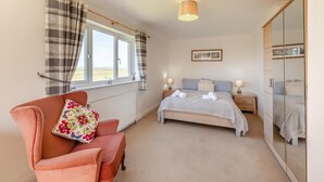 A bedroom with a bed, bedside tables, a chair, a radiator, a window with curtains, a ceiling light, and a wardrobe. - 5 Bed in Bideford (oc-codar) (Westward Ho!)