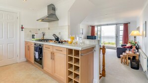 A modern kitchen with a central island, built-in oven, and a dining area with a view. - 3 Bed in Newquay (oc-headl) (Newquay)