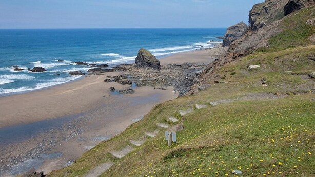 Eine Küstenlandschaft mit Strand, felsigen Klippen und blauem Himmel.