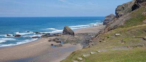 A coastal landscape with a beach, rocky cliffs, and a clear sky.