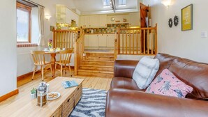 A cozy living room with a brown leather sofa, a wooden coffee table, and a kitchen in the background. - 1 Bed in Holsworthy (oc-gblue) (Holsworthy Hamlets)