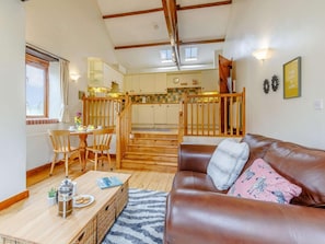 A cozy living room with a brown leather sofa, a wooden coffee table, and a kitchen in the background. - 1 Bed in Holsworthy (oc-gblue) (Holsworthy Hamlets)