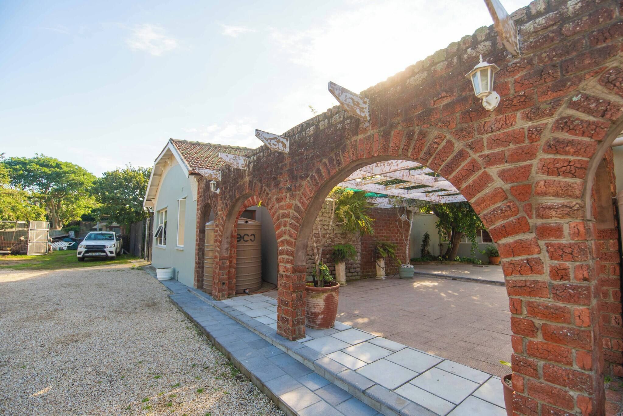 Um arco de tijolos que leva a uma casa com garagem, uma entrada de cascalho e um vaso de planta.