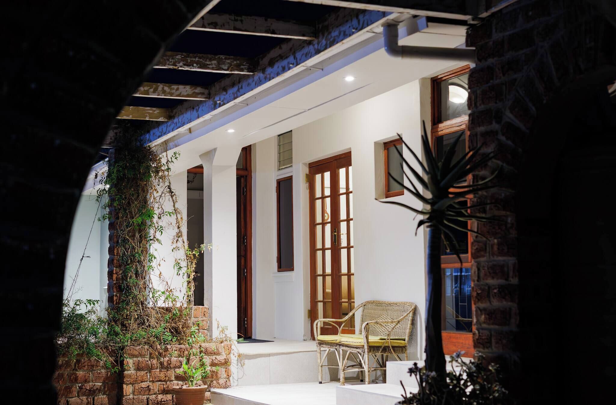 A covered outdoor area with a brick wall, a wicker chair, and a potted plant.