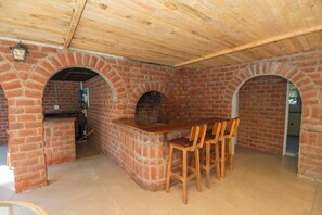 A brick-built outdoor kitchen area with a wooden table and chairs, a brick oven, and a wooden ceiling. - The Valley Guesthouse - Cottage 2 (Gqeberha)
