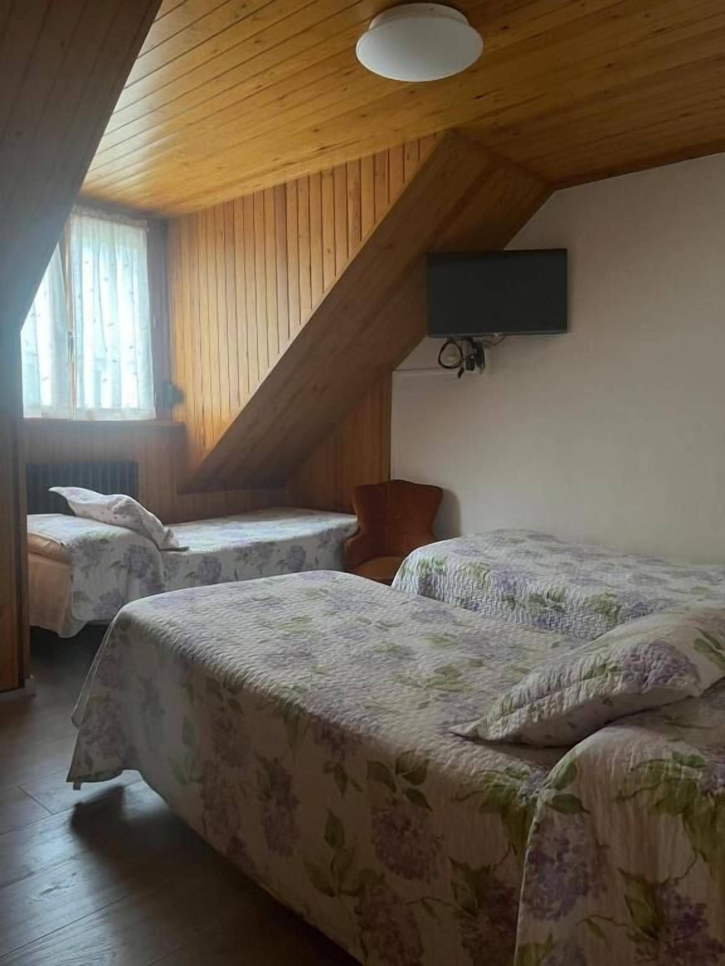 Una habitación con dos camas, vigas de madera en el techo, un televisor de pared y una ventana con cortinas.