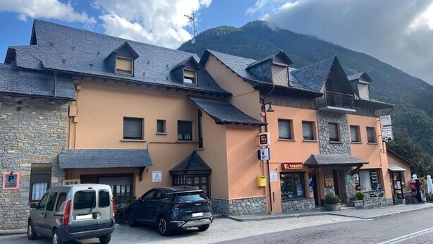 A hotel with a stone facade, multiple balconies, and a mountain backdrop.