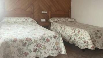Una habitación con dos camas, paredes de madera, un ventanal pequeño y una lámpara fijada a la pared.