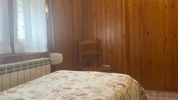 A room with wooden walls, a bed with a floral bedspread, a radiator, a chair, and a wall-mounted TV.