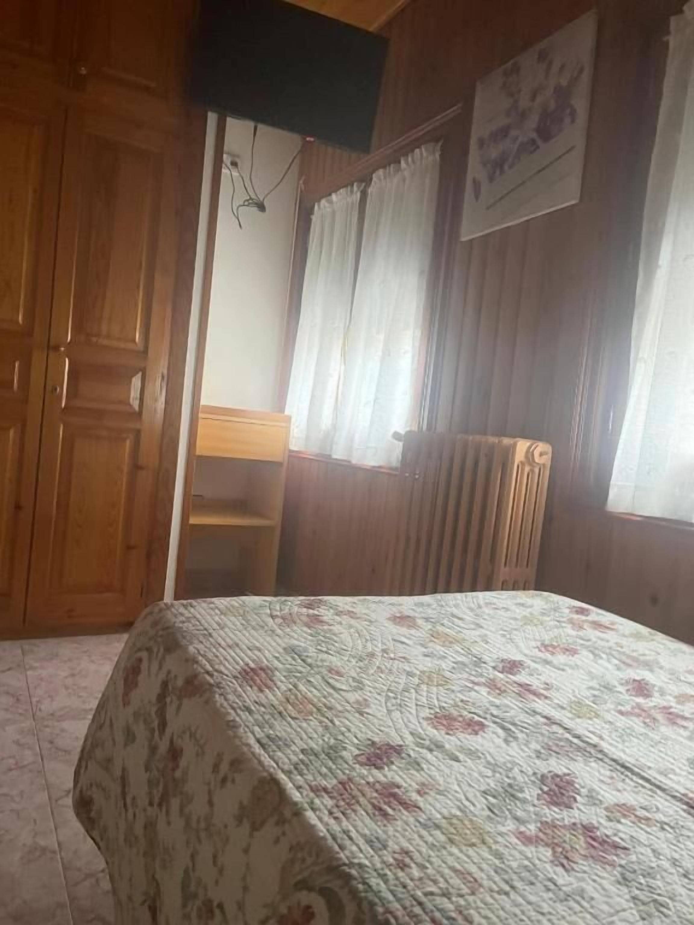 Una habitación con cama, armario de madera, escritorio y radiador.