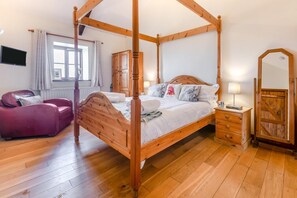 A four-poster bed with a wooden frame, a red leather sofa, a wooden nightstand with a lamp, and a wooden wardrobe. - 1 Bed in Penzance (oc-henst) (Saint Buryan)