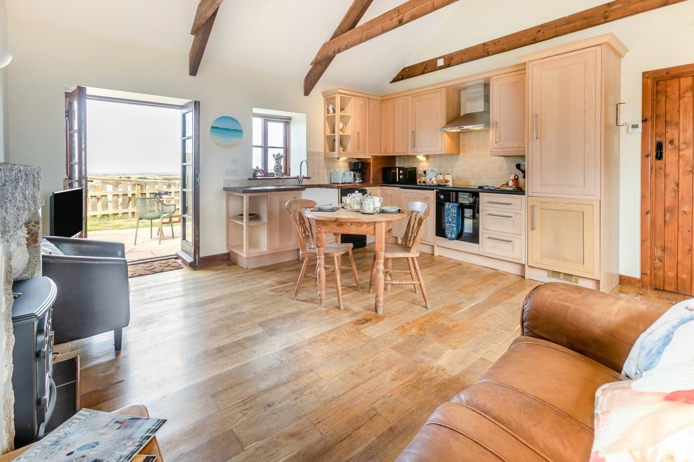 A spacious living area with a wooden floor, a dining table with chairs, a sofa, and a kitchen with wooden cabinets and a stove.