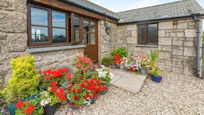 A stone building with multiple windows and a door, surrounded by a gravel driveway and various potted plants. - 1 Bed in Penzance (oc-henst) (Saint Buryan)