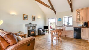 A cozy living room with a leather sofa, a fireplace, and a dining area with wooden chairs. - 1 Bed in Penzance (oc-henst) (Saint Buryan)