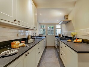 A kitchen with white cabinets, a black countertop, and a view through a door to an outdoor area. - 4 Bed in Bideford (oc-docho) (Appledore)
