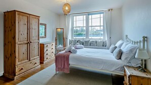 Een slaapkamer met een bed, een houten garderobe, een dressoir, een spiegel en een raam met gordijnen.