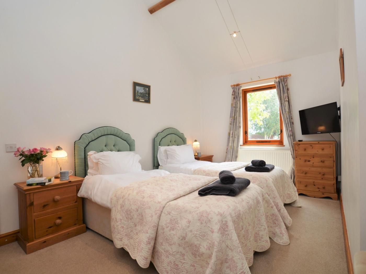 A bedroom with two beds, a wooden dresser, a television, and a window with curtains.
