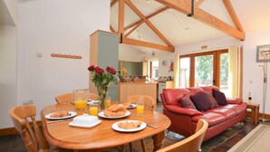 A dining area with a wooden table and chairs, a red leather sofa, and a kitchen in the background. - 2 Bed in Sherborne (oc-folwo) (Folke)