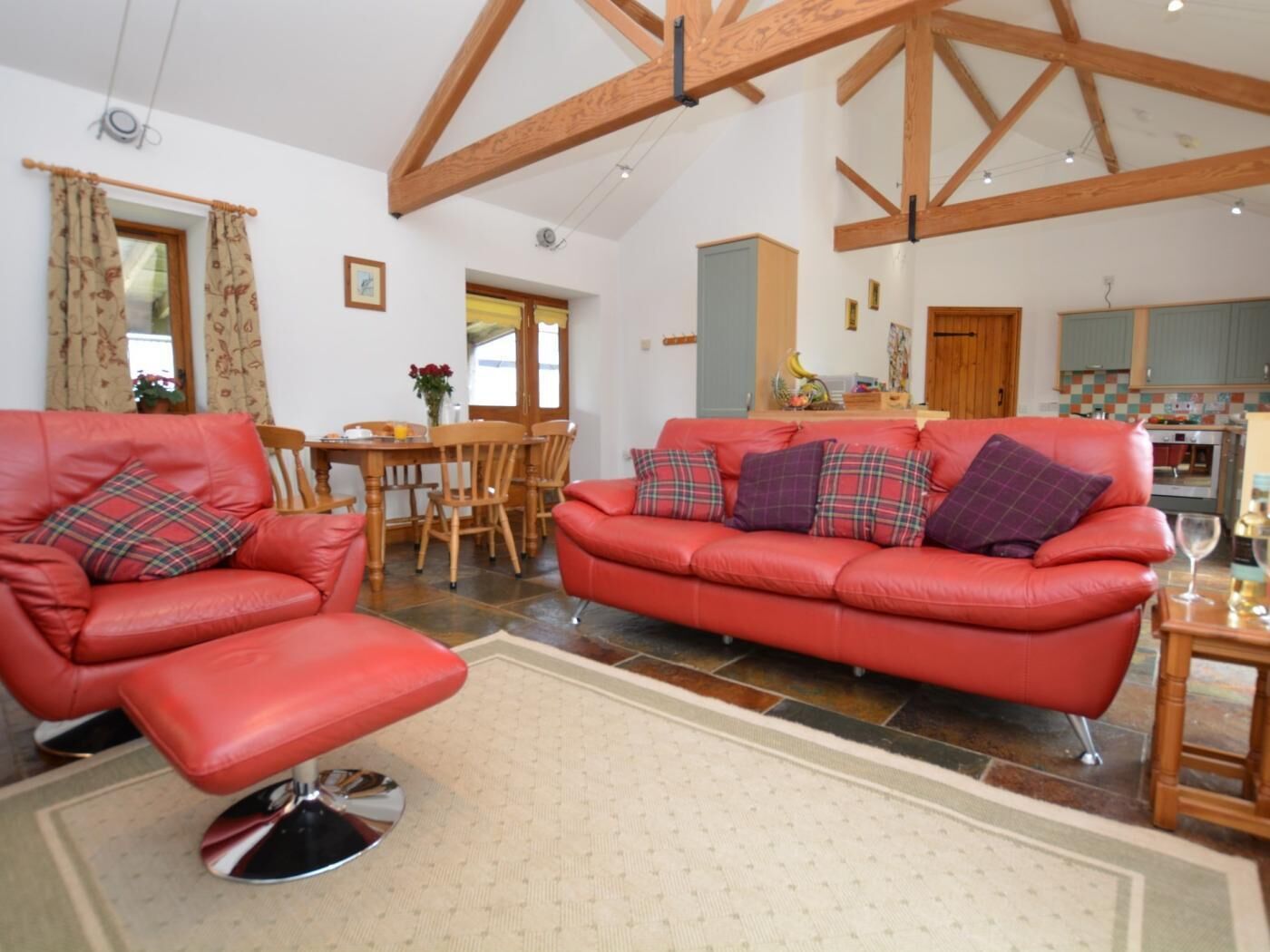 A living room with a red sofa, a red armchair, a dining table with chairs, and a kitchen in the background.