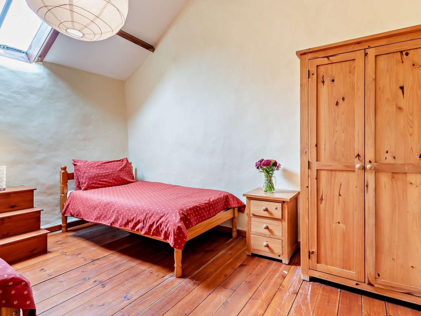 Ein Schlafzimmer mit einem hölzernen Bett, einem Nachttisch, einem Kleiderschrank und einem Oberlicht.