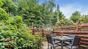 An outdoor patio with a table and chairs, surrounded by greenery and a wooden fence. - 2 Bed in Ilfracombe (oc-maltc) (West Down)