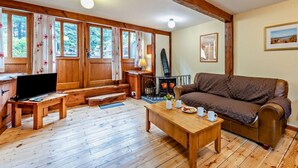 A cozy living room with a wooden floor, a sofa, a TV, a fireplace, and large windows with curtains. - 2 Bed in Ilfracombe (oc-maltc) (West Down)