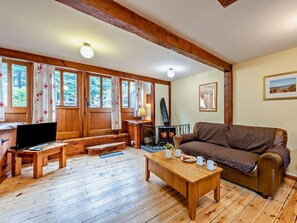 A cozy living room with a wooden floor, a sofa, a TV, a fireplace, and large windows with curtains. - 2 Bed in Ilfracombe (oc-maltc) (West Down)