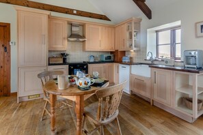 A kitchen with wooden cabinets, a dining table with chairs, a microwave, a kettle, and a coffee maker. - 1 Bed in Penzance (oc-ducks) (Saint Buryan)
