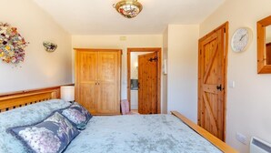 Une chambre à coucher comprenant un lit, une armoire en bois, une porte donnant accès à une salle de bain et une horloge fixée au mur.