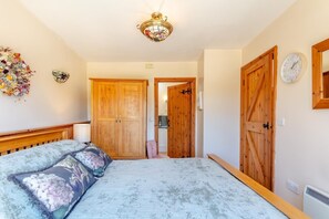 A bedroom with a bed, wooden wardrobe, a door leading to a bathroom, and a wall-mounted clock.