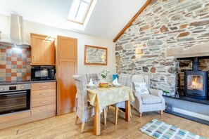 A cozy kitchen with wooden cabinets, a stone wall, and a fireplace.