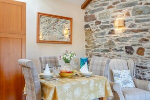 A dining area with a stone wall, wooden door, and a table set for four with chairs. - 1 Bed in Tavistock (oc-colch) (Gulworthy)