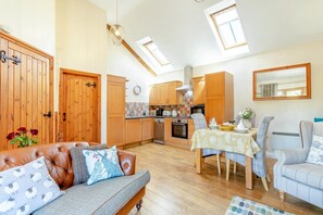 A cozy living room with a sofa, a dining table with chairs, and a kitchen area with wooden cabinets and a stove. - 1 Bed in Tavistock (oc-colch) (Gulworthy)