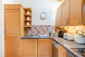 A compact kitchen with wooden cabinets, a tiled backsplash, a sink, a coffee maker, a toaster, and a kettle.