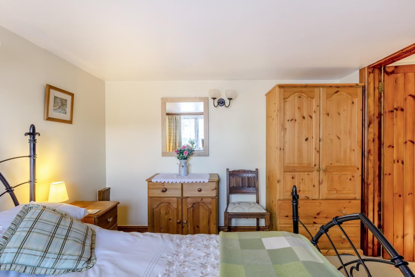 A bedroom with a bed, a wooden dresser, a nightstand, a chair, a wooden wardrobe, and a mirror.